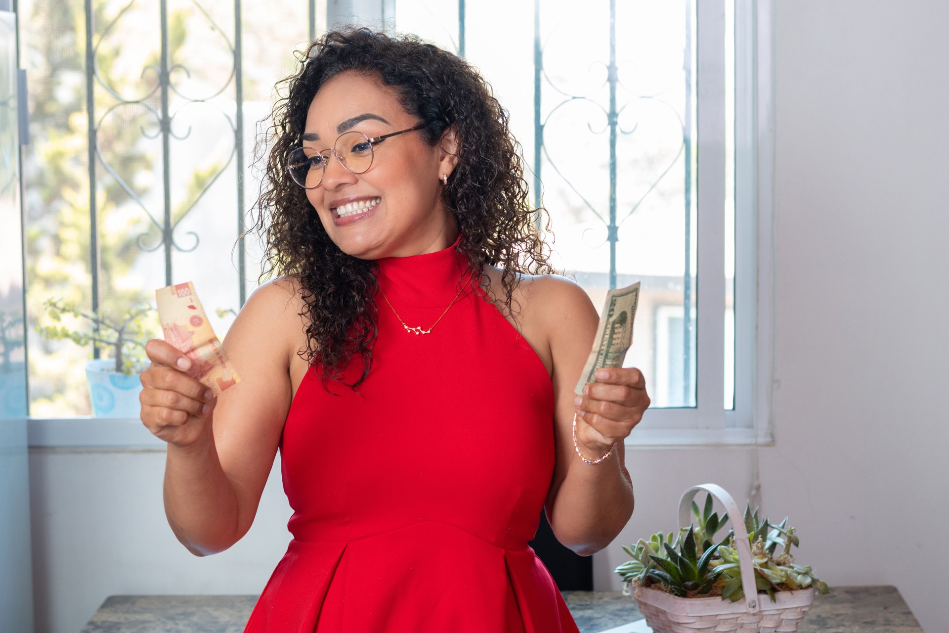 Happy latina woman holding and comparing Mexican hundred peso bill and American dollar bill. binational economy concept