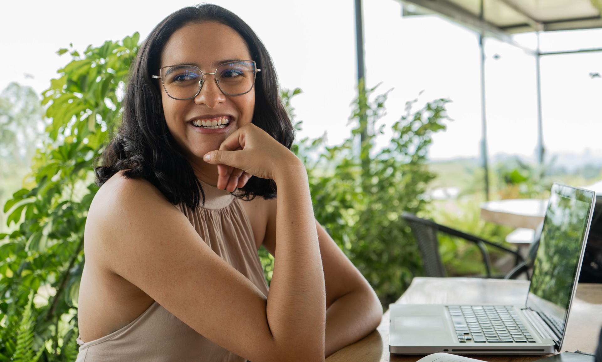 young latina woman smiling and wearing glasses looking to the side with her laptop